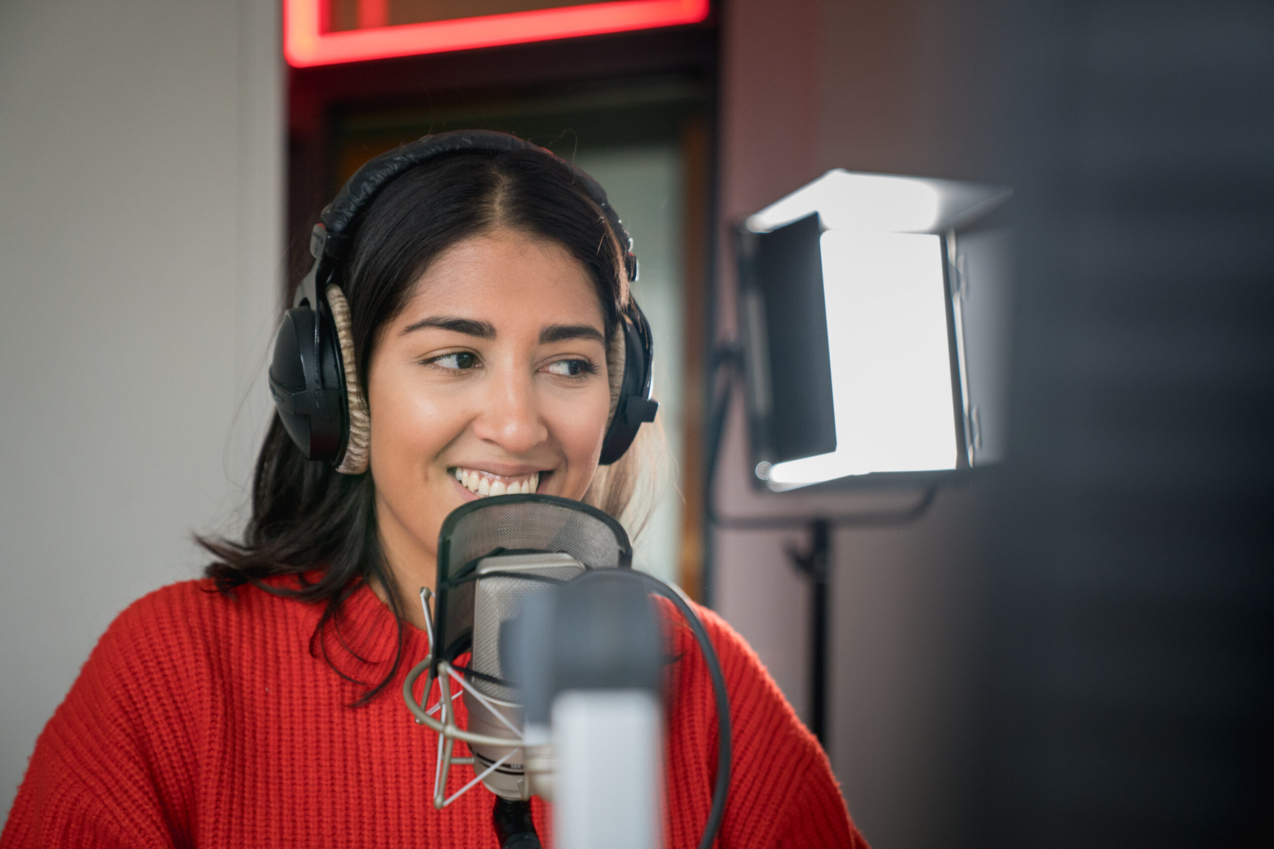 Junge Frau steht mit Kopfhörern im Radiostudio und moderiert.