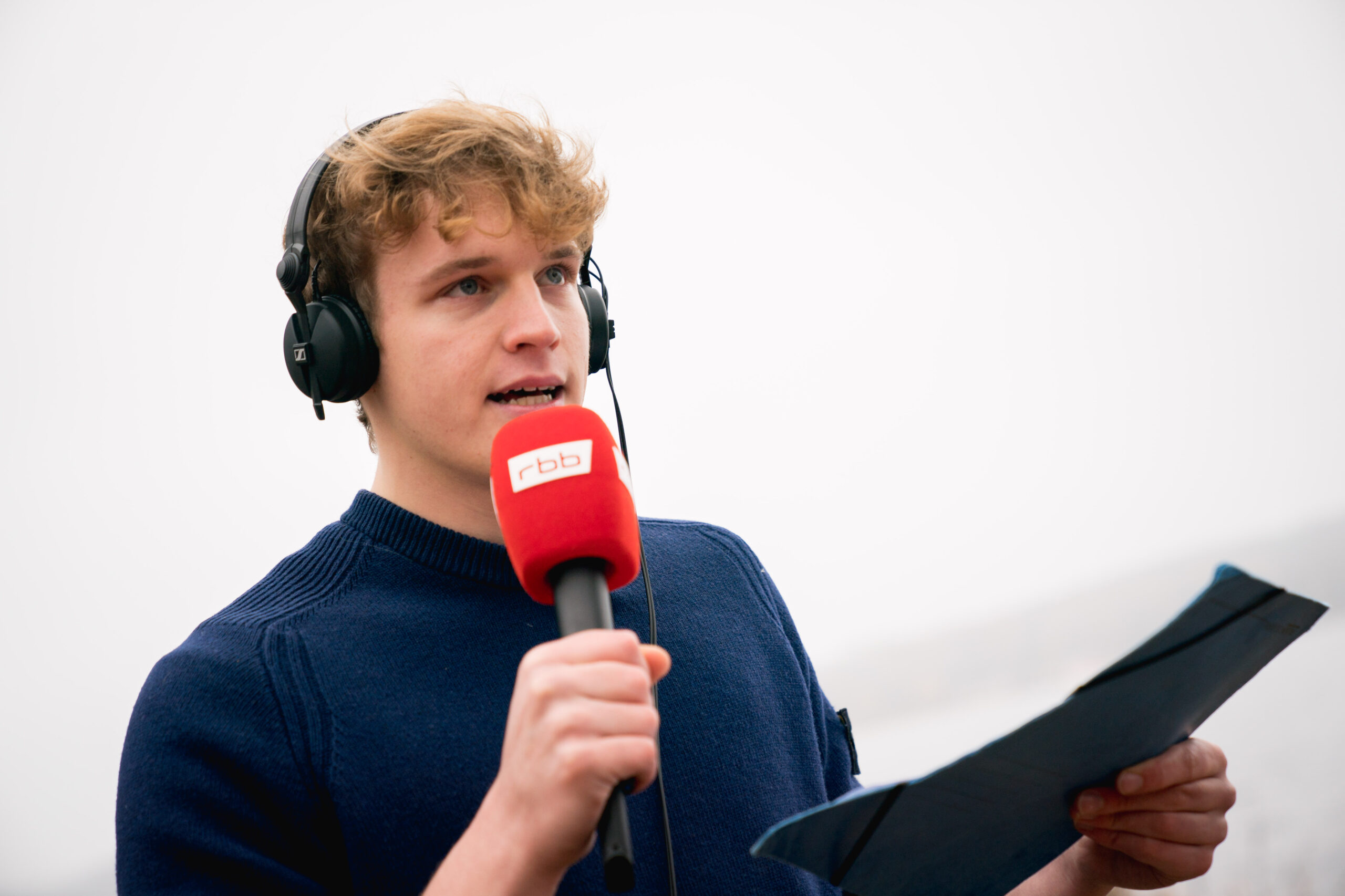 Junger Mann mit rbb-Mikrofon und Kopfhörern spricht für eine Radioliveschalte